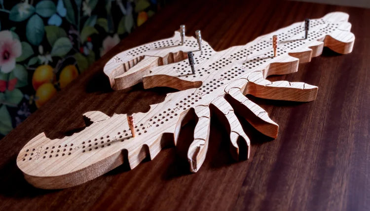 Wooden lobster-shaped cribbage board on a wooden surface with a colorful background.