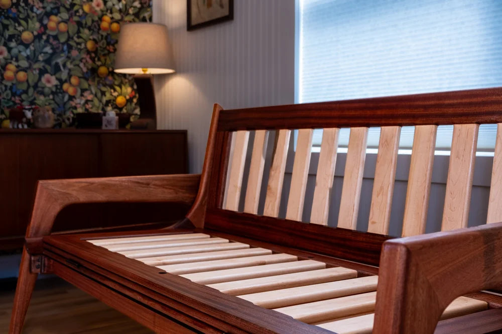 Wooden bed with slatted design in a room with a lamp and window.