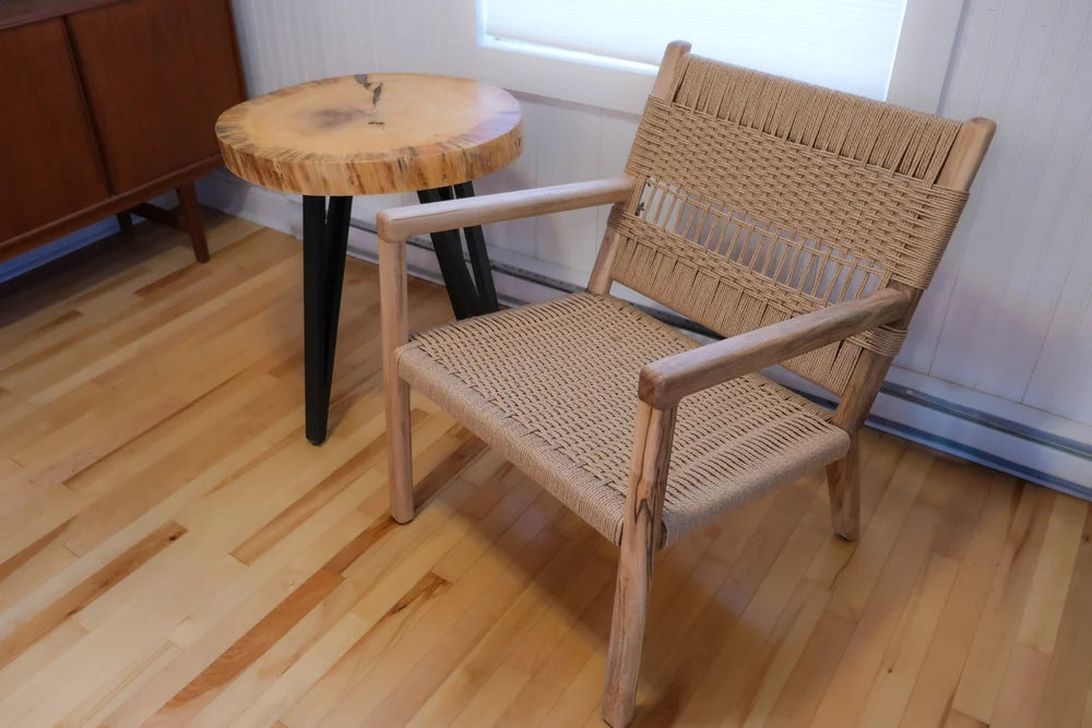 Woven chair on a wooden floor with a small round table in the background.