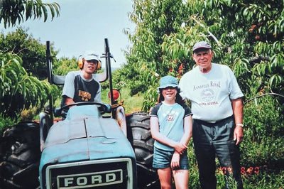 Three people standing next to a Ford tractor in an orchard.