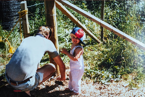 Child playing outdoors with an adult near a wooden structure.