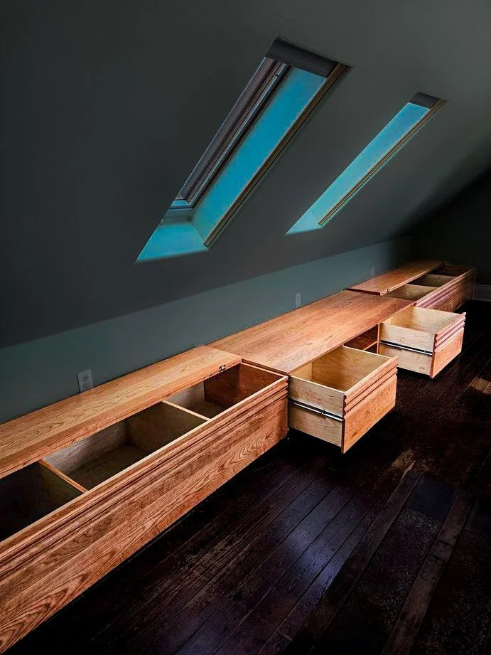 Wooden storage bench with built-in drawers against a dark wall with skylights.