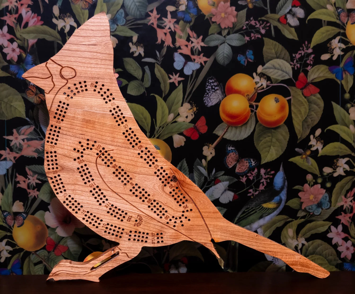 Wooden bird-shaped cribbage board on a floral background