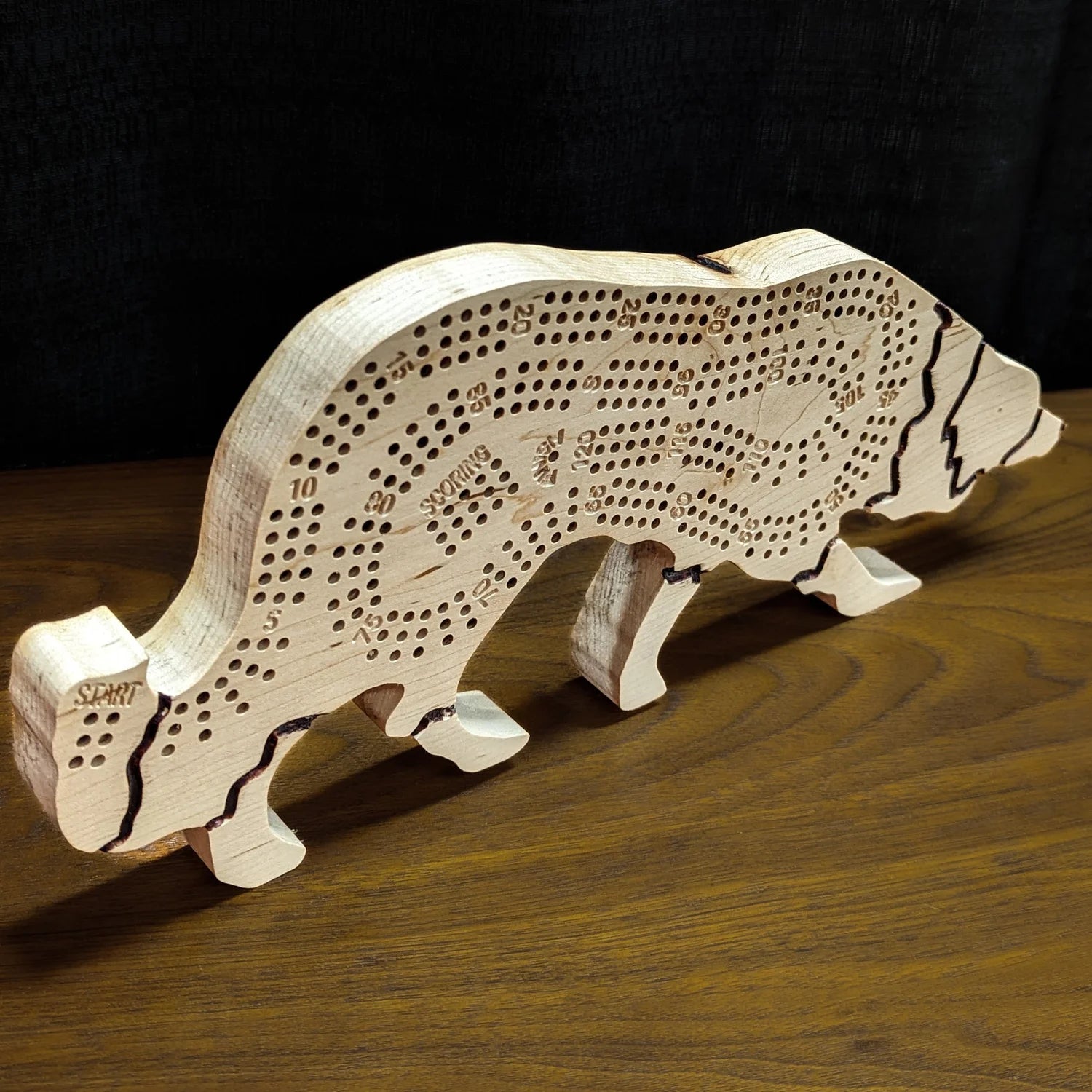 Wooden dog-shaped cribbage board on a wooden surface with a dark background