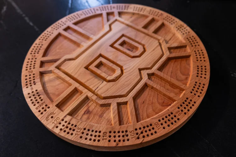 Wooden cribbage board with Bruins symbol on a dark surface