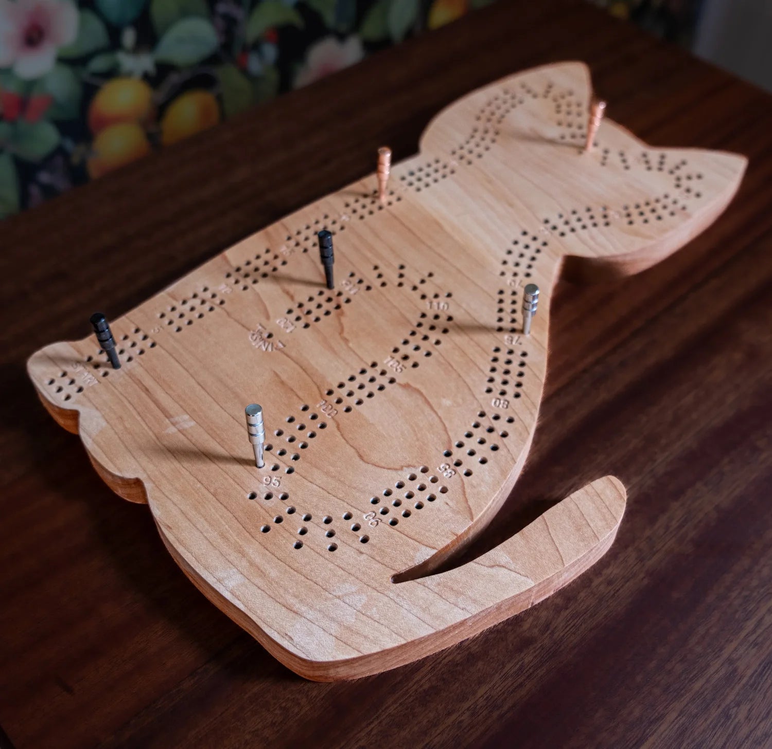 Wooden cat-shaped cribbage board on a wooden surface with a colorful background.
