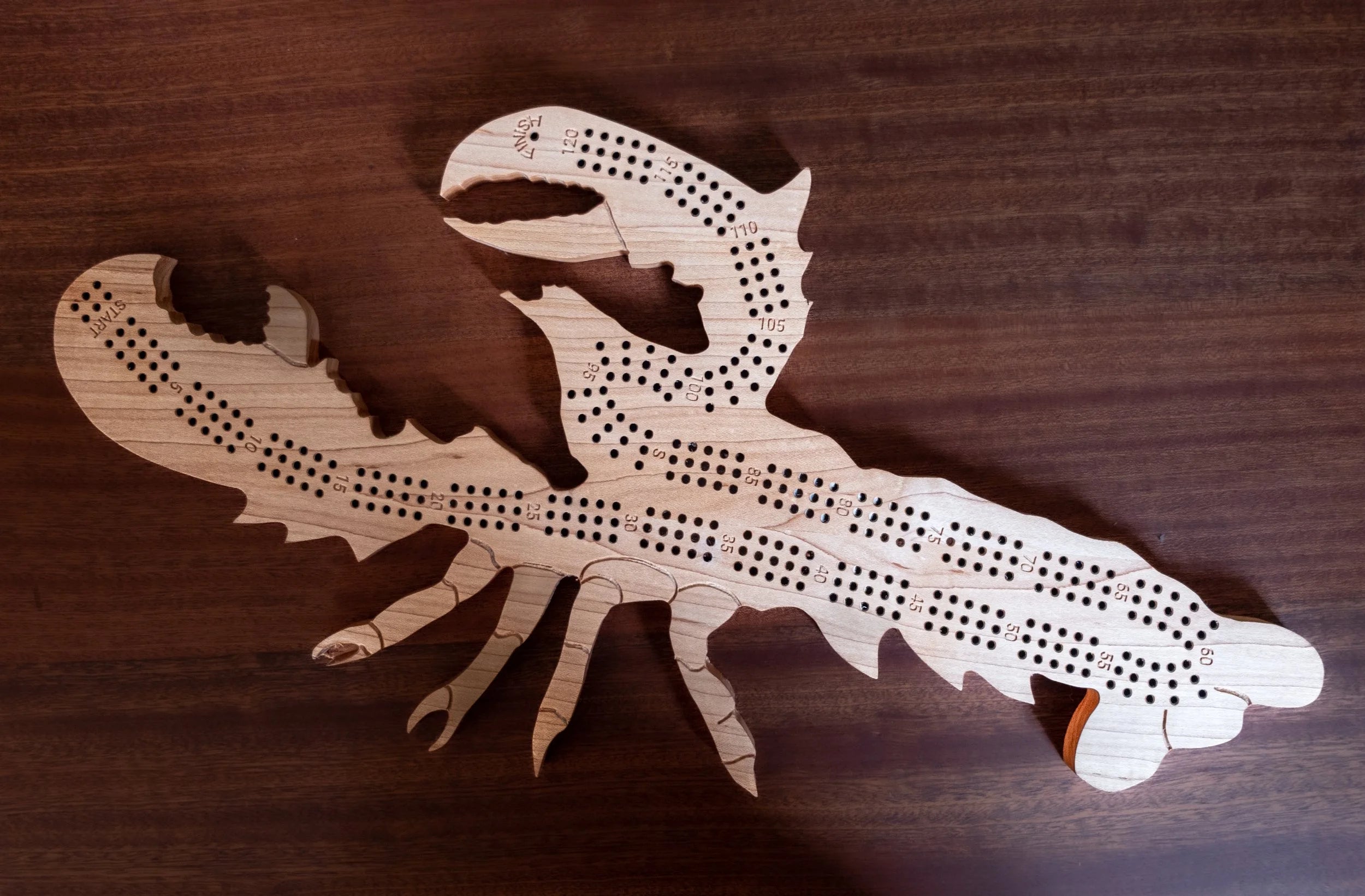 Wooden lobster-shaped cribbage board on a wooden surface