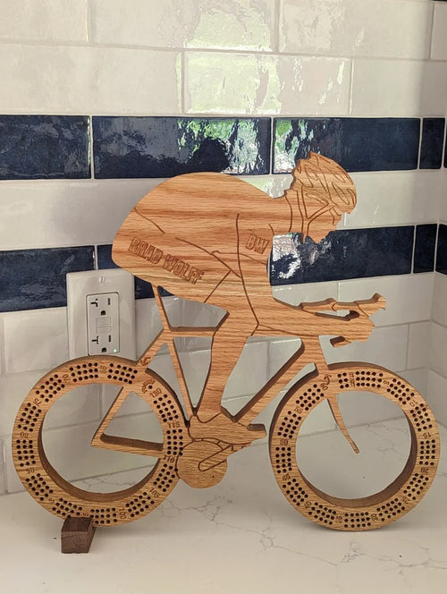 Wooden sculpture of a cyclist on a bike against a tiled wall.