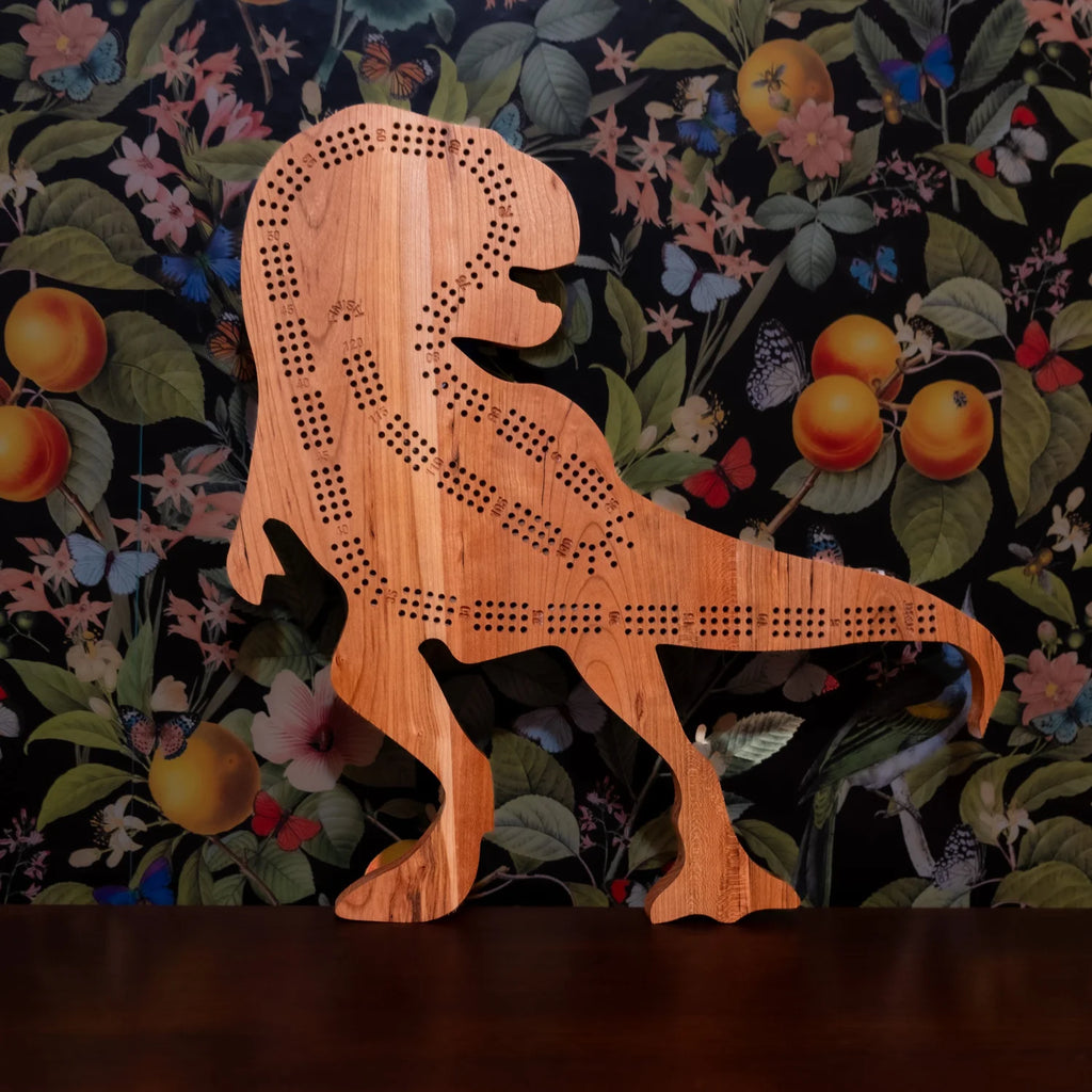 Wooden dinosaur-shaped cribbage board on a floral-patterned background
