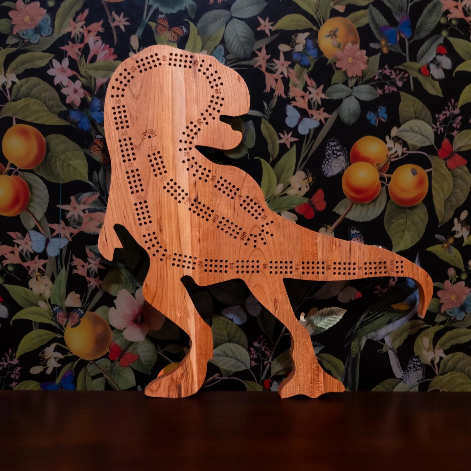 Wooden dinosaur-shaped cribbage board on a floral-patterned background
