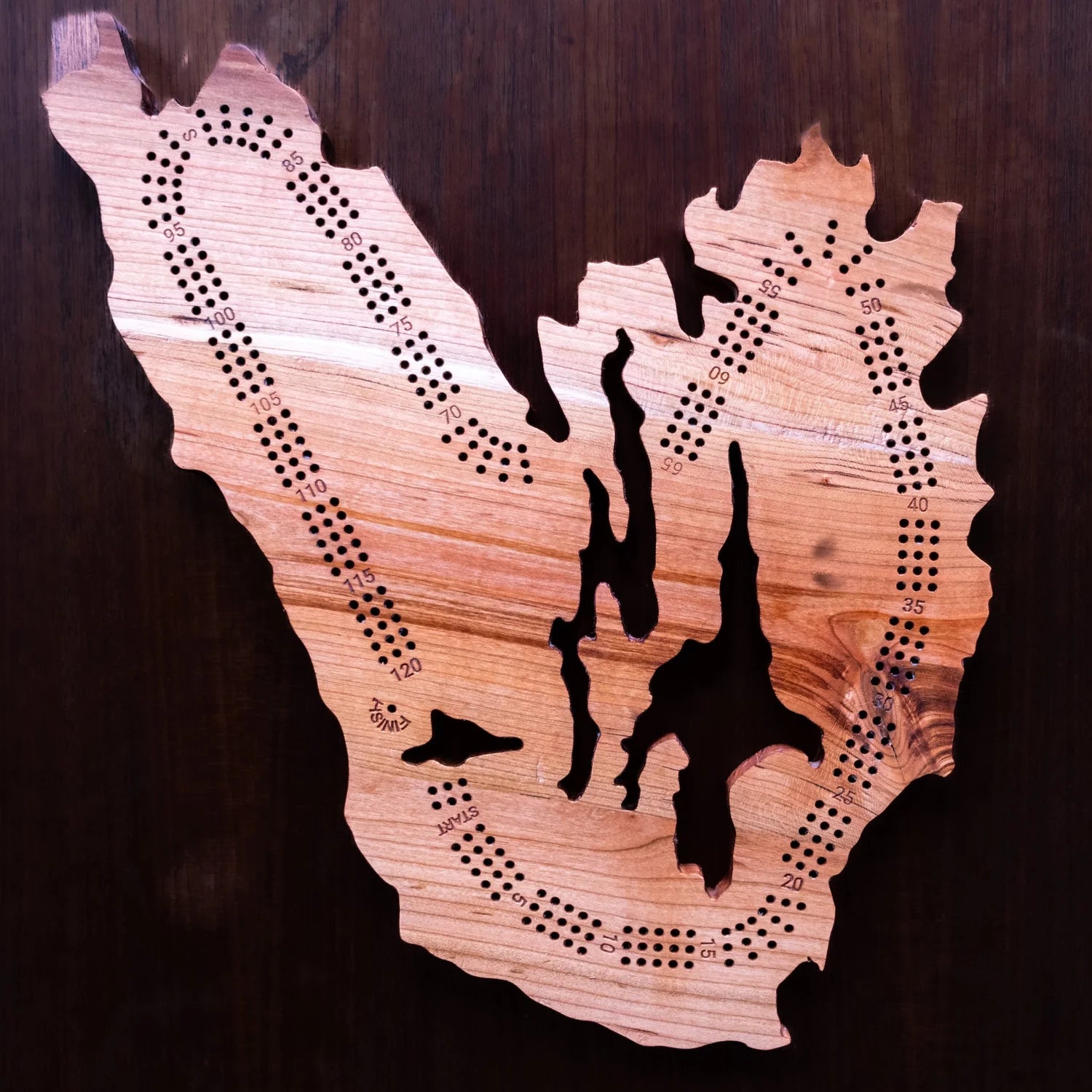Wooden cribbage board shaped like Cape Breton on a dark background