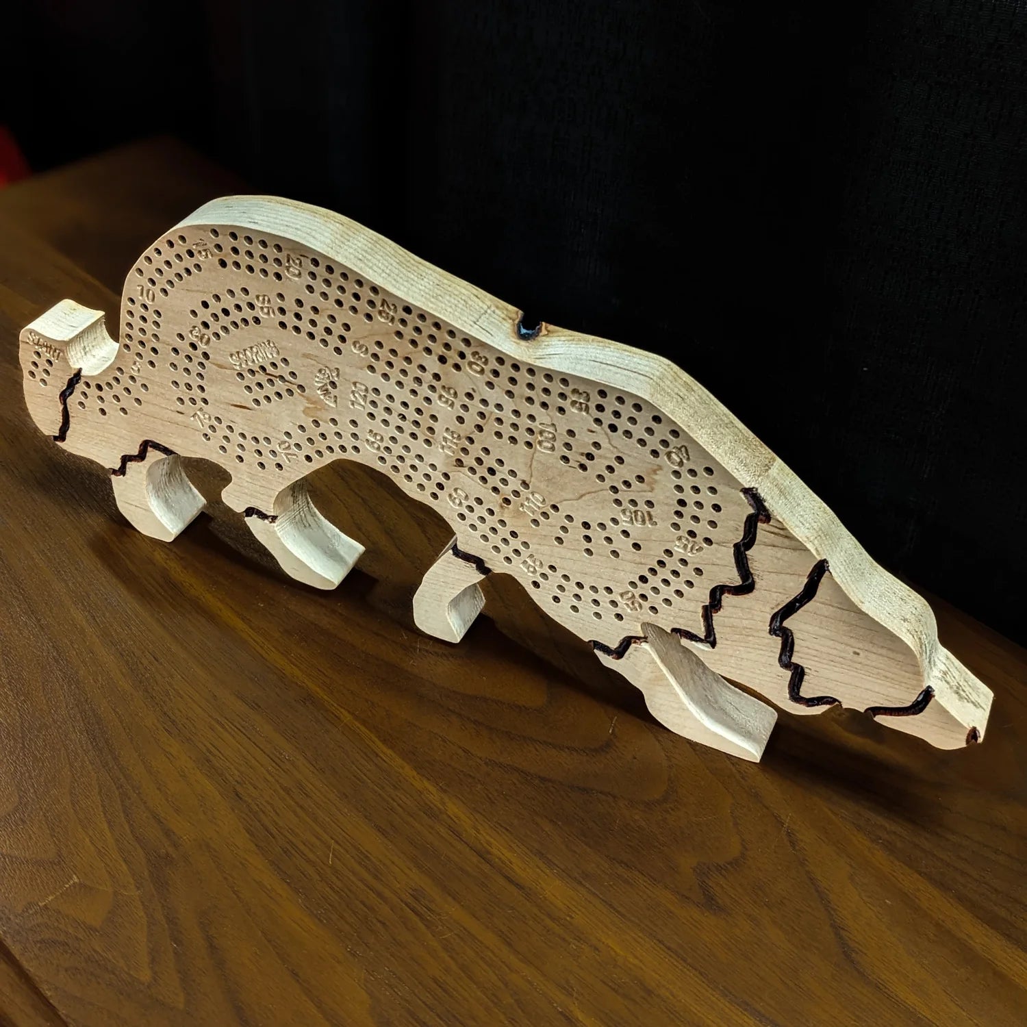 Wooden dog-shaped cribbage board on a wooden surface with a dark background