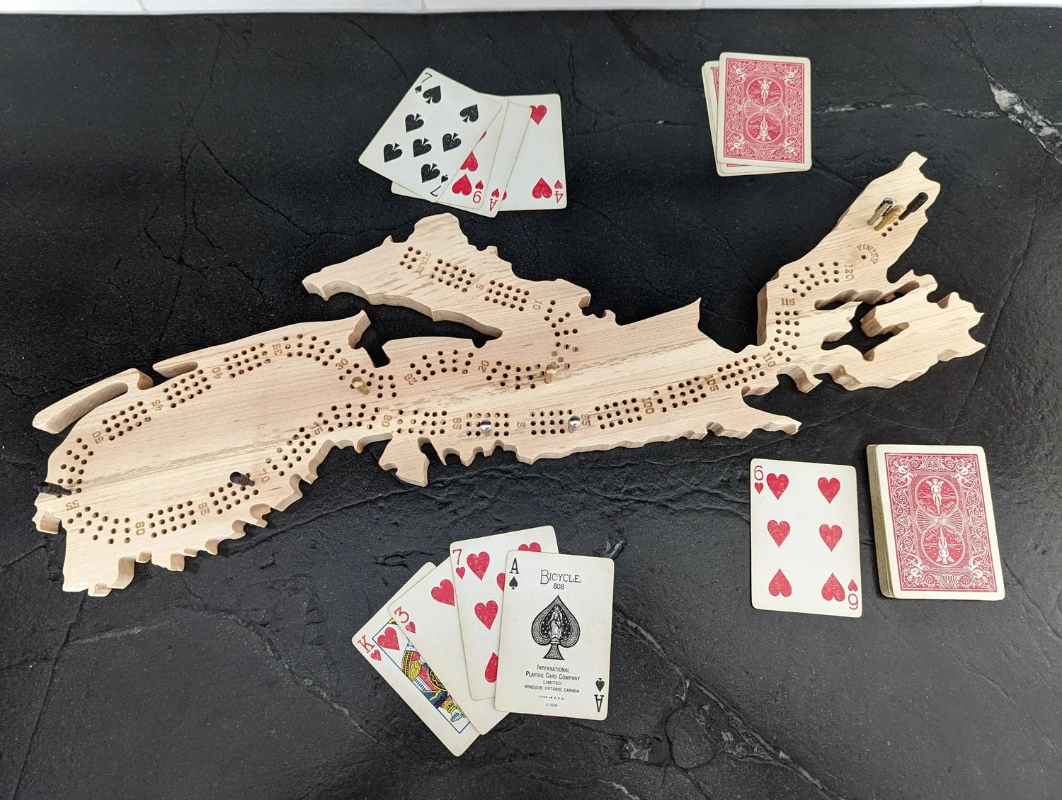 Wooden cribbage board with playing cards on a dark surface