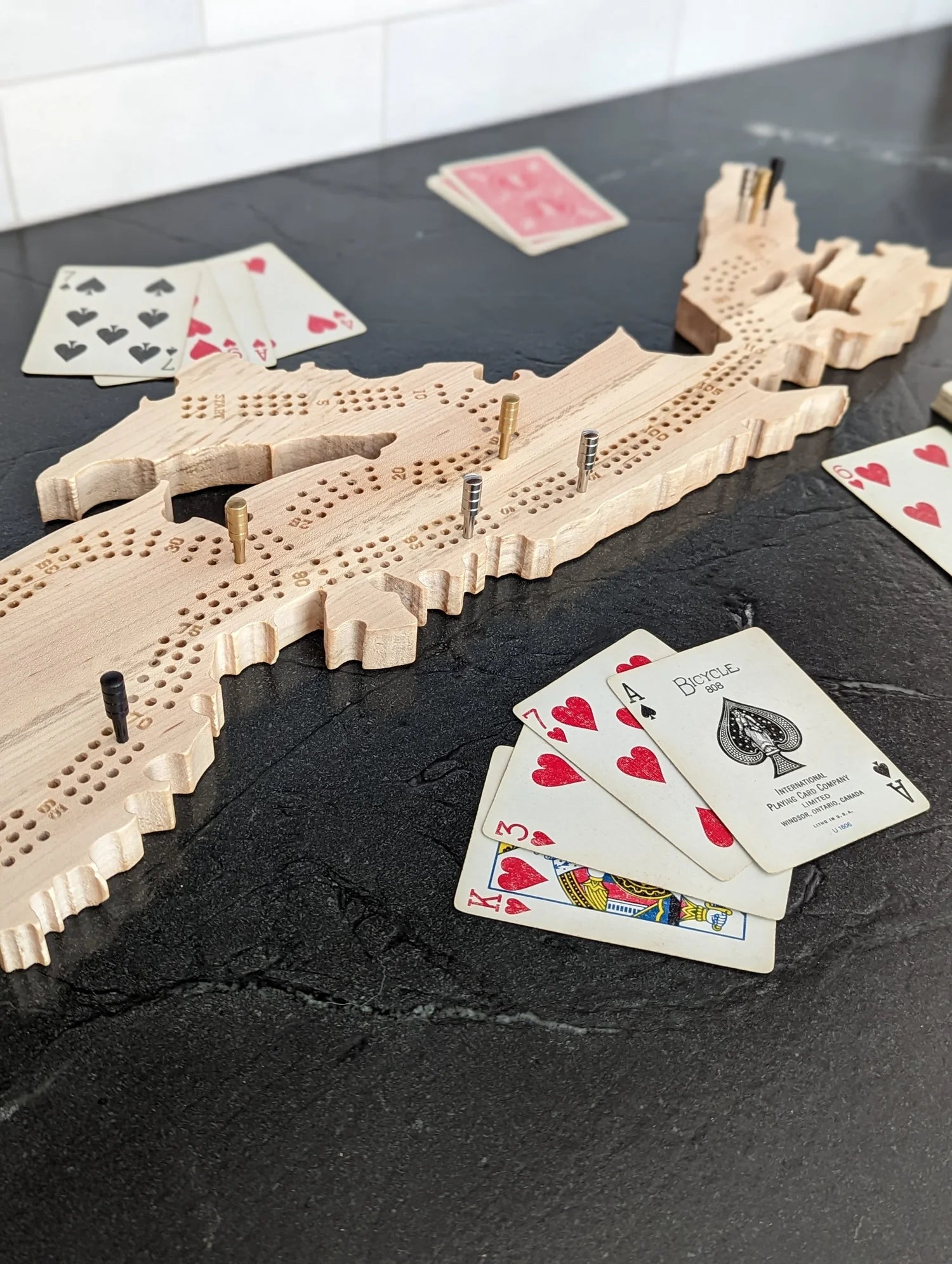 Wooden Nova Scotia shaped cribbage board with playing cards on a dark surface