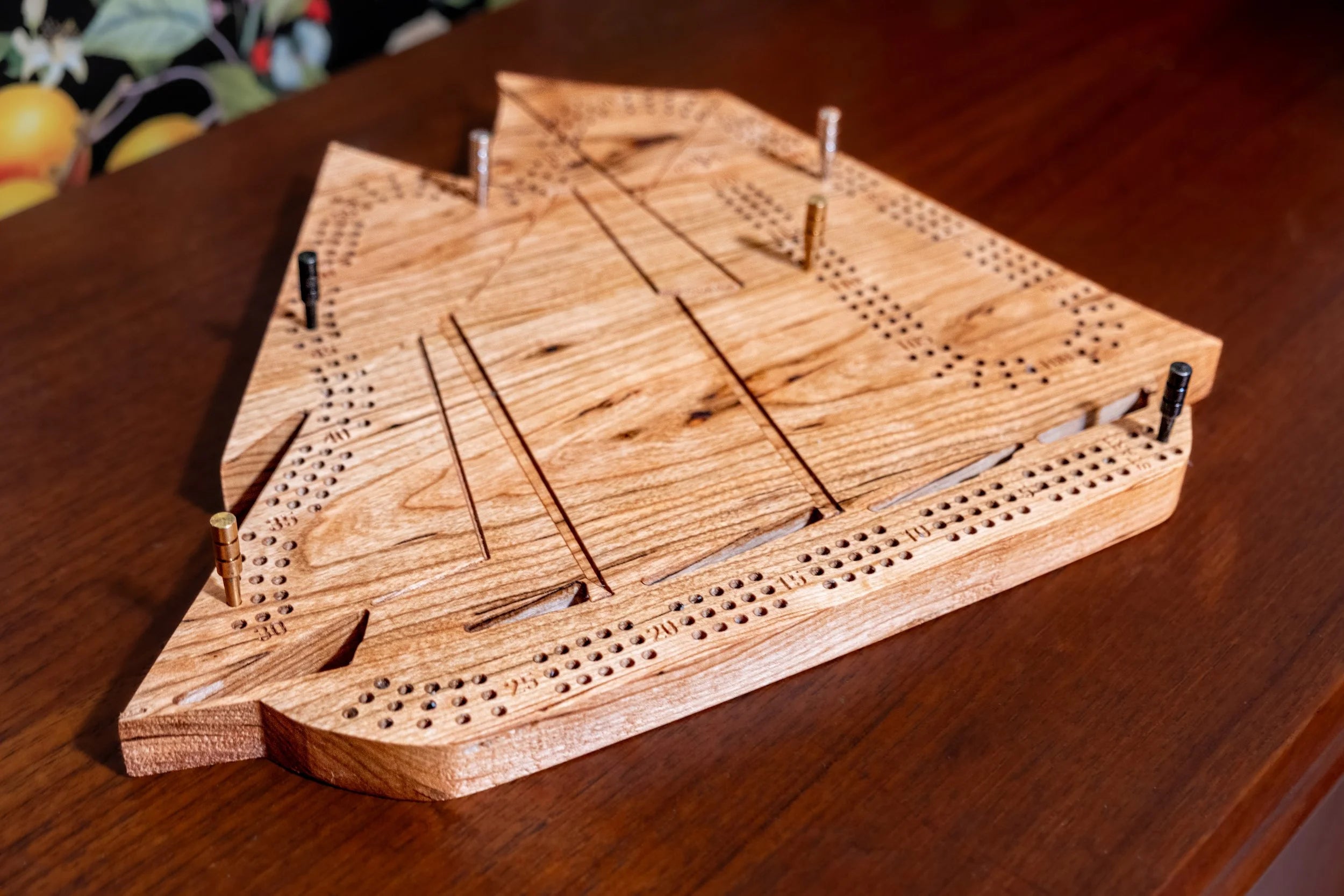 Wooden cribbage board on a wooden surface with fruits in the background